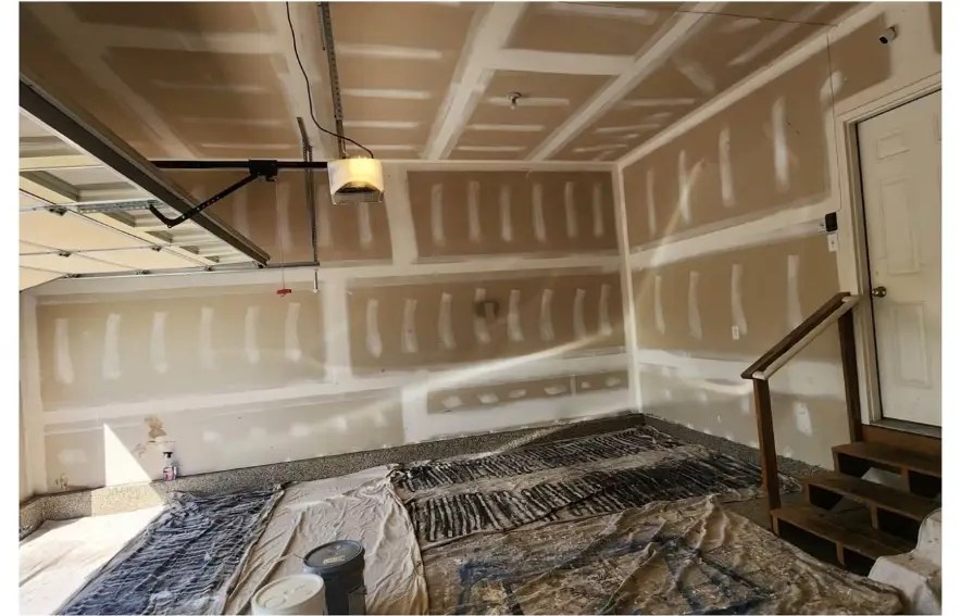 Before garage painting: bare and patched drywall with tarps on the epoxy floor